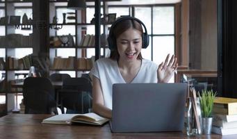 Une adolescente asiatique souriante étudie dans une bibliothèque avec des livres d'ordinateur portable faisant des recherches en ligne pour les cours, prenant des notes pour les devoirs de dissertation, concept d'apprentissage en ligne de l'éducation en ligne photo