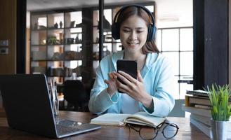 belle étudiante universitaire asiatique du millénaire écoutant de la musique avec ses écouteurs sans fil modernes et utilisant un smartphone. photo