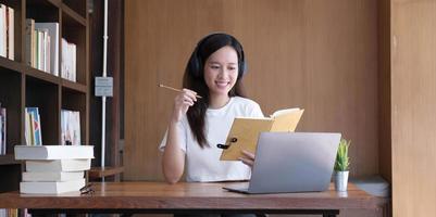 une femme asiatique portant des écouteurs étudie en ligne en regardant un podcast de webinaire sur un ordinateur portable en écoutant l'apprentissage de l'éducation par conférence téléphonique, concept d'apprentissage en ligne. photo