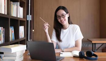 Une jeune étudiante asiatique intelligente se sent satisfaite pendant les cours en ligne sur Internet et vous sourit à la maison photo