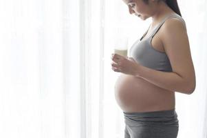 jeune femme enceinte buvant du lait à la maison, soins de santé et soins de grossesse photo