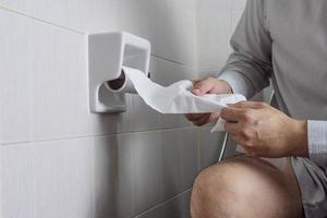 L'homme tire le tissu tout en étant assis dans la cuvette des toilettes - problème de santé de l'estomac photo