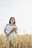 jeune femme en robe blanche debout sur un champ de blé avec le lever du soleil sur l'arrière-plan photo