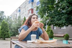 élégante femme millénaire mangeant un hamburger au café de la rue en été photo