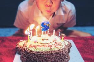 l'enfant souffle joyeusement des bougies sur son gâteau d'anniversaire - concept de célébration de fête d'anniversaire joyeuse et joyeuse photo