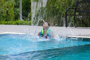 petite fille dans un gilet de sauvetage saute dans une piscine extérieure. jolie petite fille jouant dans la piscine par une journée ensoleillée. concept de style de vie d'été.