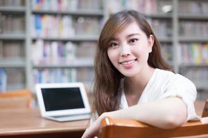 belle étudiante asiatique utilisant un ordinateur portable pour étudier dans la bibliothèque photo