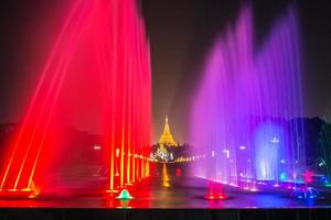 le spectacle de la fontaine colorée dans le parc du peuple avec vue sur la pagode shwedagon à yangon, myanmar la nuit. photo