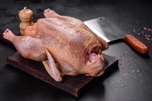 dinde crue ou poulet avec sel, épices et herbes sur une planche à découper en bois. préparer une table de fête photo