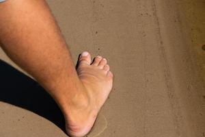 la jambe droite et le pied d'un homme nu se dressent sur le sable du littoral. photo