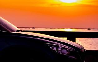 vue latérale d'une voiture suv au design sportif et moderne garée sur une route en béton au bord de la plage de la mer au coucher du soleil. technologie des voitures hybrides et électriques. voyage en voiture. industrie automobile. ciel orange et jaune. photo