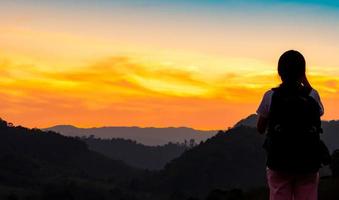 vue arrière de la jeune femme regardant le beau coucher de soleil sur la couche de montagne. routard heureux de voyager seul. silhouette de randonnée touristique au sommet de la montagne. activité d'aventure de fille active. photo