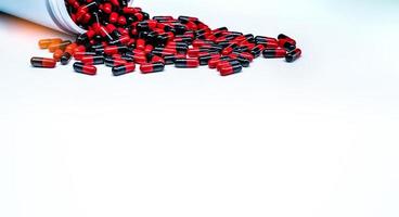 pilules de capsule antibiotique rouge-noir réparties dans une bouteille de médicament en plastique sur fond blanc. résistance aux antibiotiques. industrie pharmaceutique. fabrication pharmaceutique. production de gélules. photo