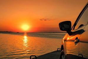 voiture suv compacte bleue au design sportif et moderne garée sur une route en béton au bord de la mer au coucher du soleil. technologie respectueuse de l'environnement. concept de réussite commerciale. photo