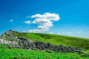 paysage d'herbe verte et de colline rocheuse au printemps avec un beau ciel bleu et des nuages blancs. vue campagne ou champêtre. fond de nature en journée ensoleillée. environnement d'air frais. pierre sur la montagne. photo