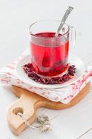 thé d'hibiscus dans une tasse en verre, planche de bois, fond de bois blanc