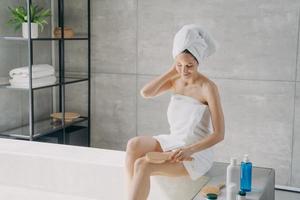 jolie fille caucasienne fait un massage du corps avec une brosse dans la salle de bain. routine de soins du corps du matin.