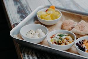 concept de plat traditionnel savoureux. plan recadré de plateau avec fromage de chèvre, pain pita, betteraves grillées dans des bols sur table en bois. nourriture israélienne photo