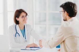 une femme médecin amicale accueille le patient avec une poignée de main, pose dans une clinique privée, s'assoit l'une en face de l'autre, discute, accepte de signer un contrat d'assurance, se rencontre à l'hôpital. concept de soins de santé et de médecine photo