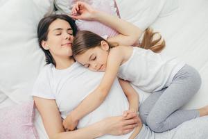 un petit enfant heureux dort près de sa mère, embrasse avec amour, fait des rêves agréables, s'allonge sur un lit confortable. maman et jolie fille dorment bien dans la chambre. concept de famille, de sommeil et de repos photo