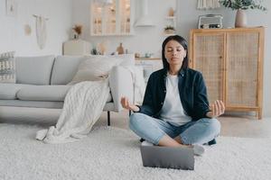 fille assise sur le sol devant un ordinateur portable en posture de lotus et écoutant de la musique tranquille dans des airpods. photo