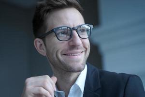 jeune entrepreneur masculin positif dans des verres et des vêtements de cérémonie regardant de côté avec un sourire agréable photo