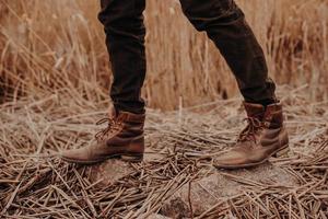 photo recadrée d'un homme méconnaissable portant de vieilles chaussures en cuir marron, pose sur le sol avec du chaume, marche seul sur le terrain.