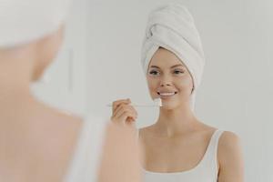 belle femme en bonne santé avec une serviette sur la tête après la douche ayant un sourire à pleines dents tout en se brossant doucement les dents photo