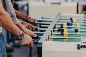 des hommes méconnaissables jouent au baby-foot, apprécient le jeu d'équipe, veulent gagner des adversaires, passent du temps libre au pub. jeu de kick. match de foot sur table photo