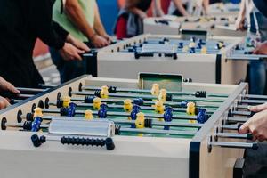 des amis masculins jouent au baby-foot avec beaucoup de chaleur, profitent de temps de loisirs ou de loisirs, veulent gagner. centre de divertissement. joueurs en plastique colorés sur un match de football photo