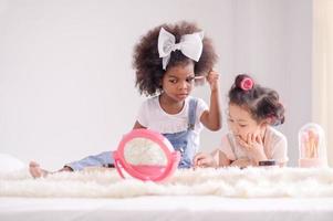 une jolie petite fille asiatique et amie africaine applique joyeusement des pinceaux de maquillage avec de la poudre dans sa chambre photo