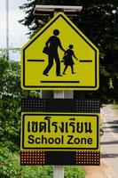 panneau de zone scolaire sur fond d'arbre et de route. photo