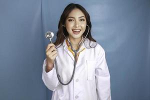 portrait d'une jeune femme médecin asiatique, un professionnel de la santé sourit et porte un stéthoscope isolé sur fond bleu photo