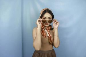 concept rétro d'une jeune femme asiatique tient ses lunettes de soleil isolées par un fond bleu photo
