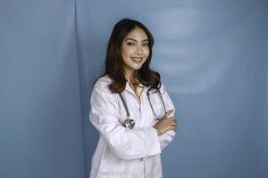 portrait d'une jolie femme médecin confiante, amicale et souriante bras croisés porter un stéthoscope de blouse de laboratoire blanc isolé sur fond bleu photo