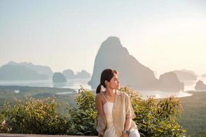 femme voyageuse heureuse profiter du point de vue de la baie de phang nga, seule touriste assise et relaxante à samet nang elle, près de phuket dans le sud de la thaïlande. concept de voyage, de voyage et de vacances d'été en asie du sud-est photo