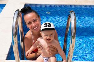 une maman heureuse en maillot de bain rouge avec son petit fils joue à l'extérieur, sur fond de piscine à l'eau bleue. photo