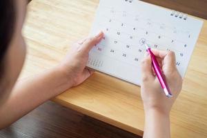 page de calendrier avec une main féminine tenant un stylo sur la table du bureau photo