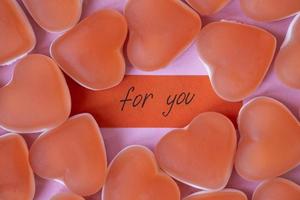 confiture de bonbons rouges en forme de coeur avec une note pour vous sur fond rose. bonbons gélifiés au sucre. notion de saint valentin. motif géométrique. design minimaliste, mise à plat, vue de dessus. photo