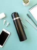 lieu de travail indépendant, café élégant boit du thermos et prend des notes, smartphone avec écouteurs et bouteille thermo en acier écologique pour l'eau. photo