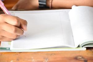 vue de face d'un étudiant asiatique tenant un stylo à la main et faisant le test en classe. concept pour tester, écrire et faire des devoirs et des devoirs. mise au point sélective sur la main et le stylo. photo