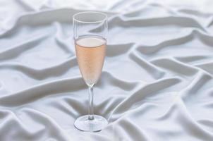 un verre de vin rosé sur un tissu satiné ondulé. rester à la maison. photo