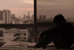 l'homme assis sur le lit avec vue sur la ville depuis la chambre. photo