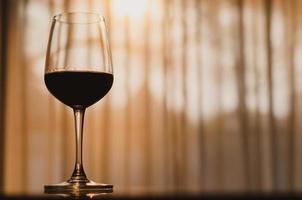 un verre de vin rouge sur la table dans la chambre avec la lumière du coucher du soleil sur fond curtien. photo