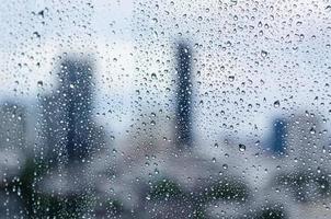 goutte de pluie sur la fenêtre en verre pendant la journée pendant la saison de la mousson avec un arrière-plan flou des bâtiments de la ville. photo