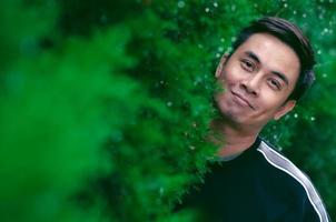 homme asiatique souriant avec un visage heureux debout dans un buisson vert pour un bon concept de santé mentale. photo