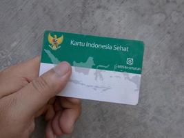 surabaya, jawa timur, indonésie, 2022 - un homme tenant une carte bpjs de santé indonésienne sur un fond gris flou photo