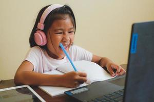 fille thaïlandaise en cours d'apprentissage en ligne à la maison pendant la situation covid-19. étudiant écrivant le livre et apprenant le cahier de formulaire pendant la quarantaine. mise au point sélectionnée. éducation en ligne, concept d'école à domicile. photo