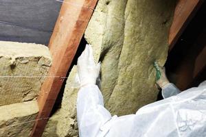 un homme dans une combinaison de protection met de la laine minérale entre la poutre du toit de la maison pour son réchauffement du froid photo