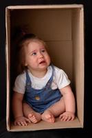 heureuse petite fille assise dans une boîte en carton et s'amusant photo